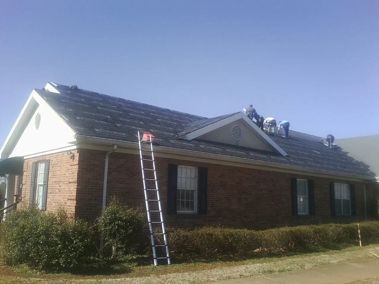 Crew tearing shingles off a brick ranch roof with a ladder set — Metal Roof Repair work by our crew in Avon By The Sea
