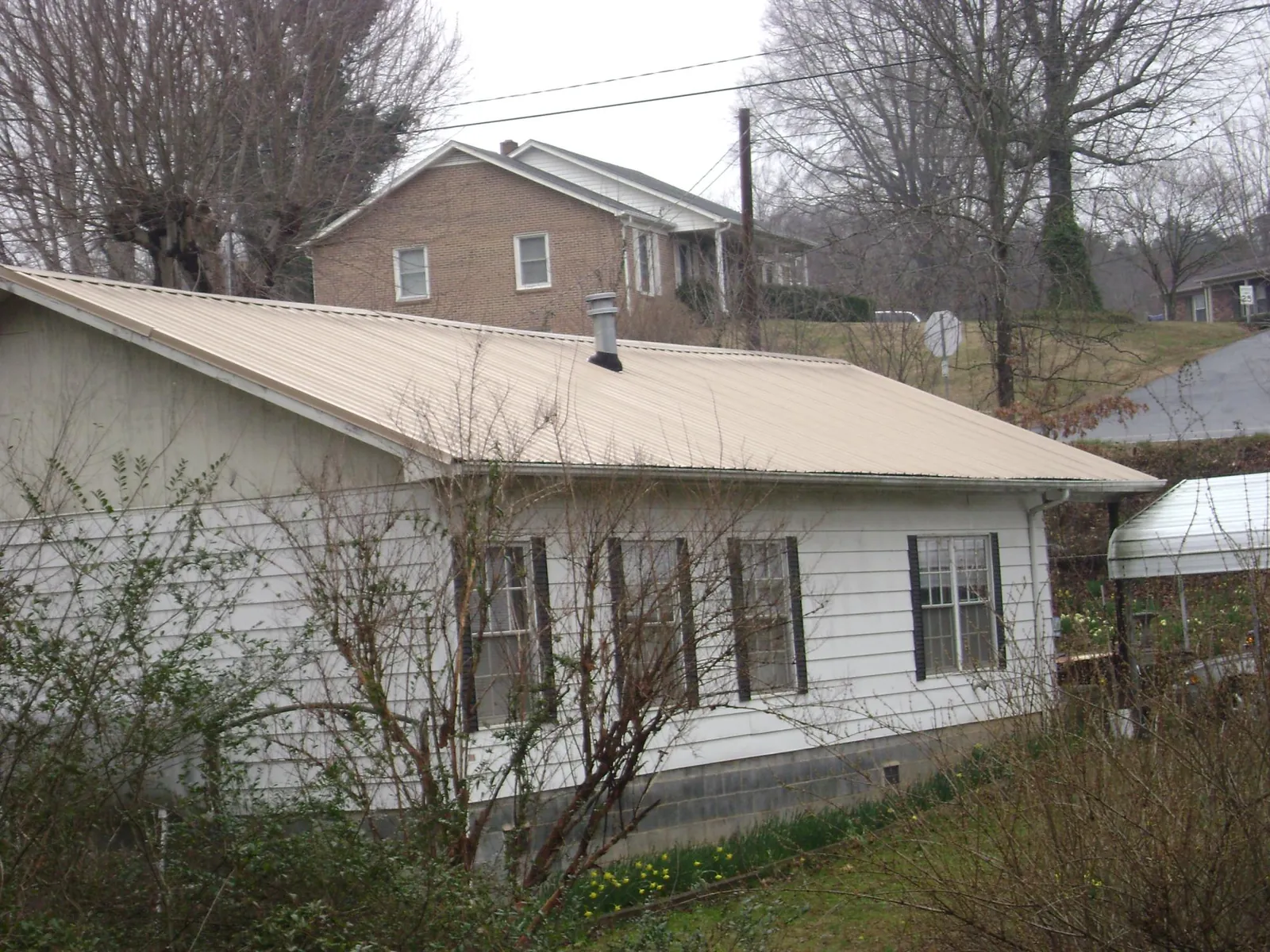 Tan metal roof on a white sided house set into a hillside — Commercial Roofing by Roofing Brothers in Avon By The Sea