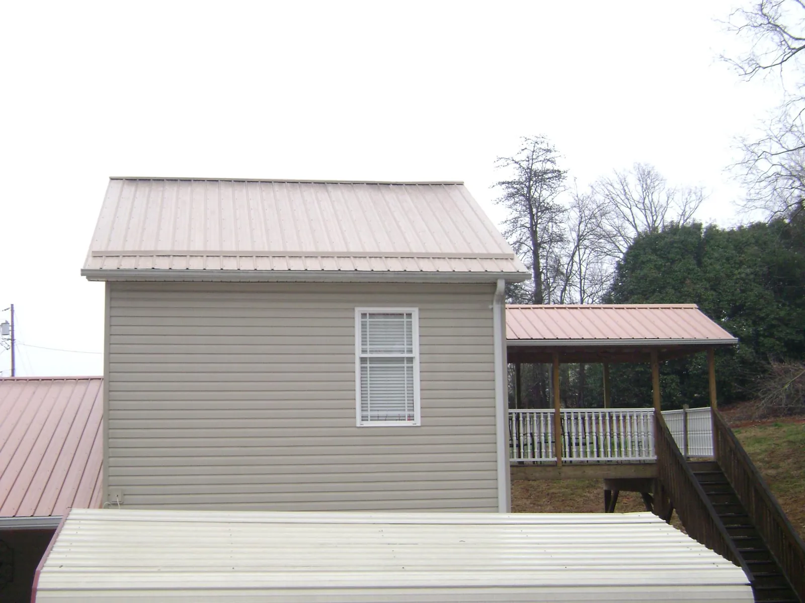 Tan metal roofs on a two story addition and attached porch, from a Roof Replacement job in Avon By The Sea